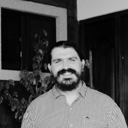 A man with a beard and glasses is smiling in a black and white photo.