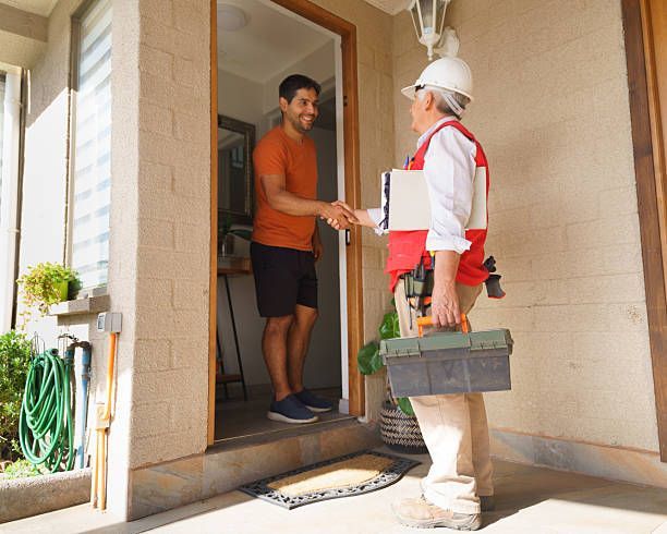 Man at doorway shakes hands with a worker in a hard hat, holding a toolbox.