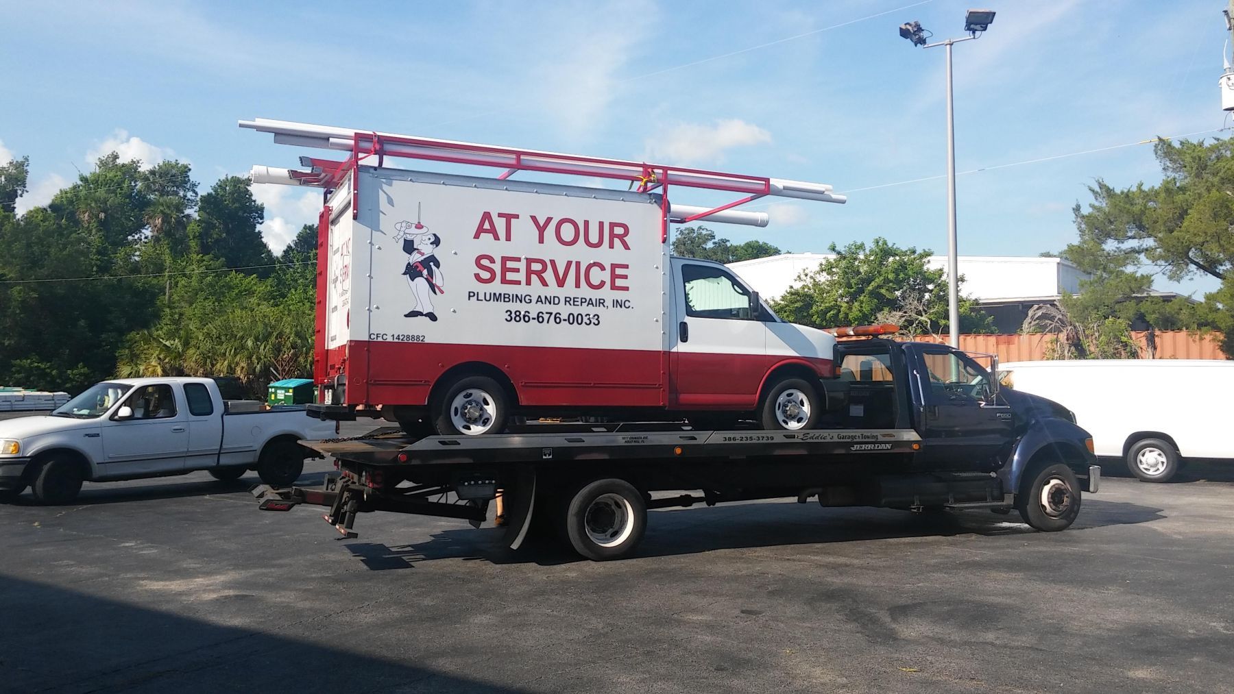 A tow truck is carrying a red and white van that says at your service