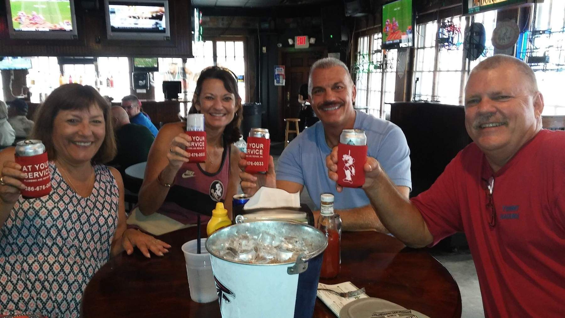 A group of people are sitting at a table holding cans of beer.