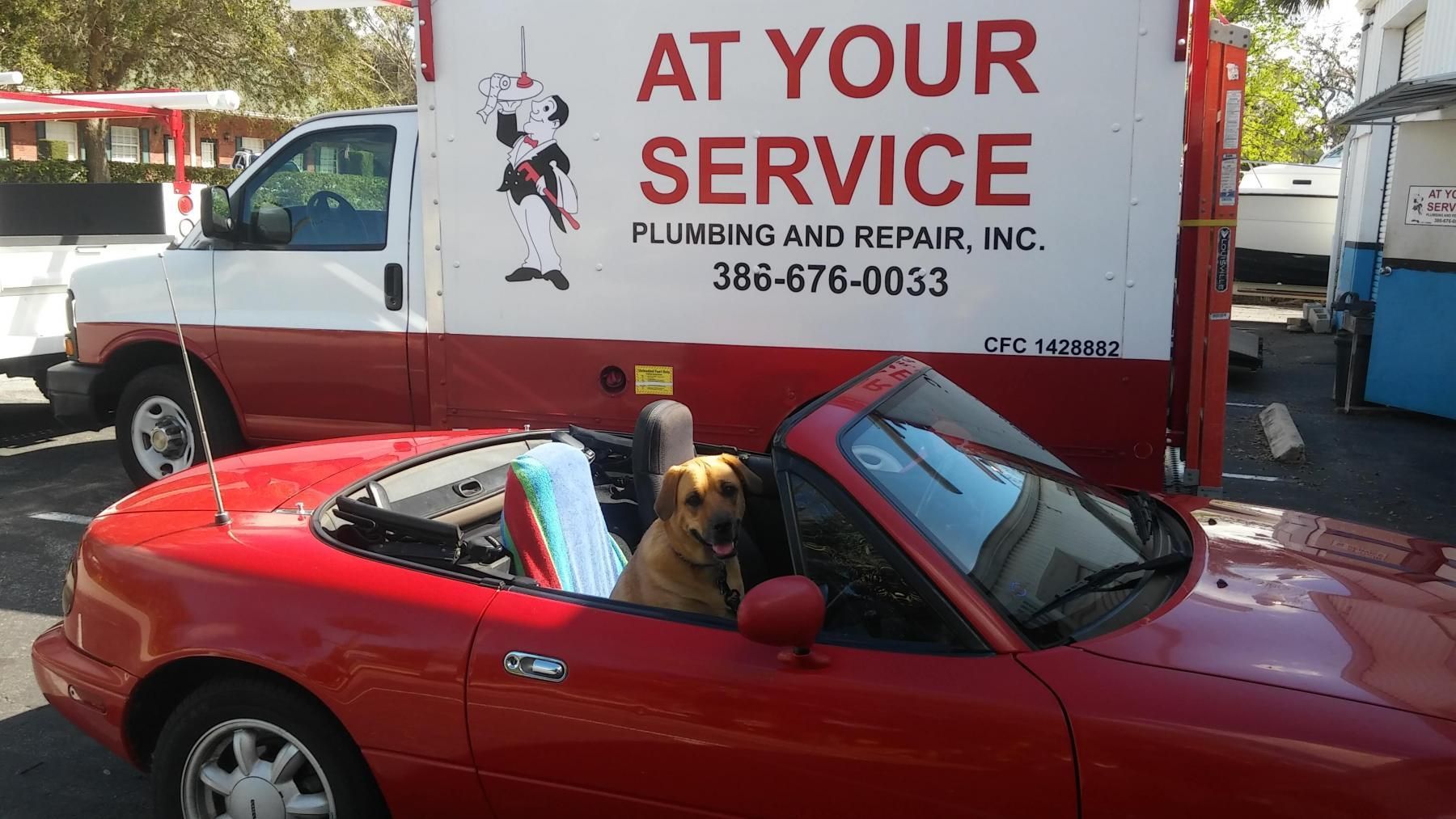 A red car is parked in front of a truck that says at your service