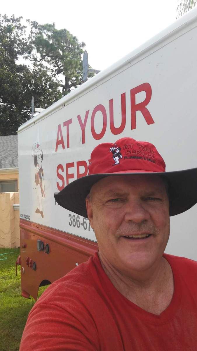 A man wearing a red hat is standing in front of a truck that says at your service