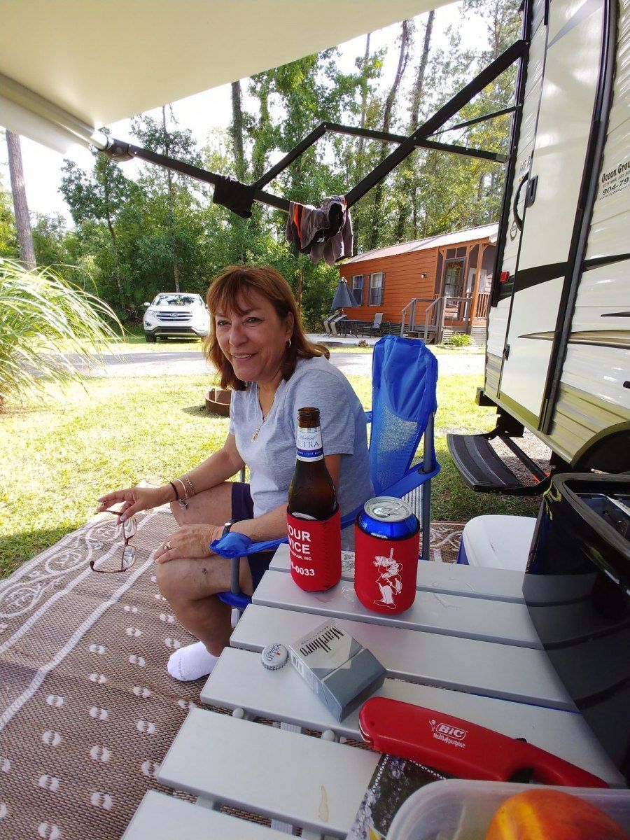 A woman is sitting at a table with a can of soda and a bottle of beer.