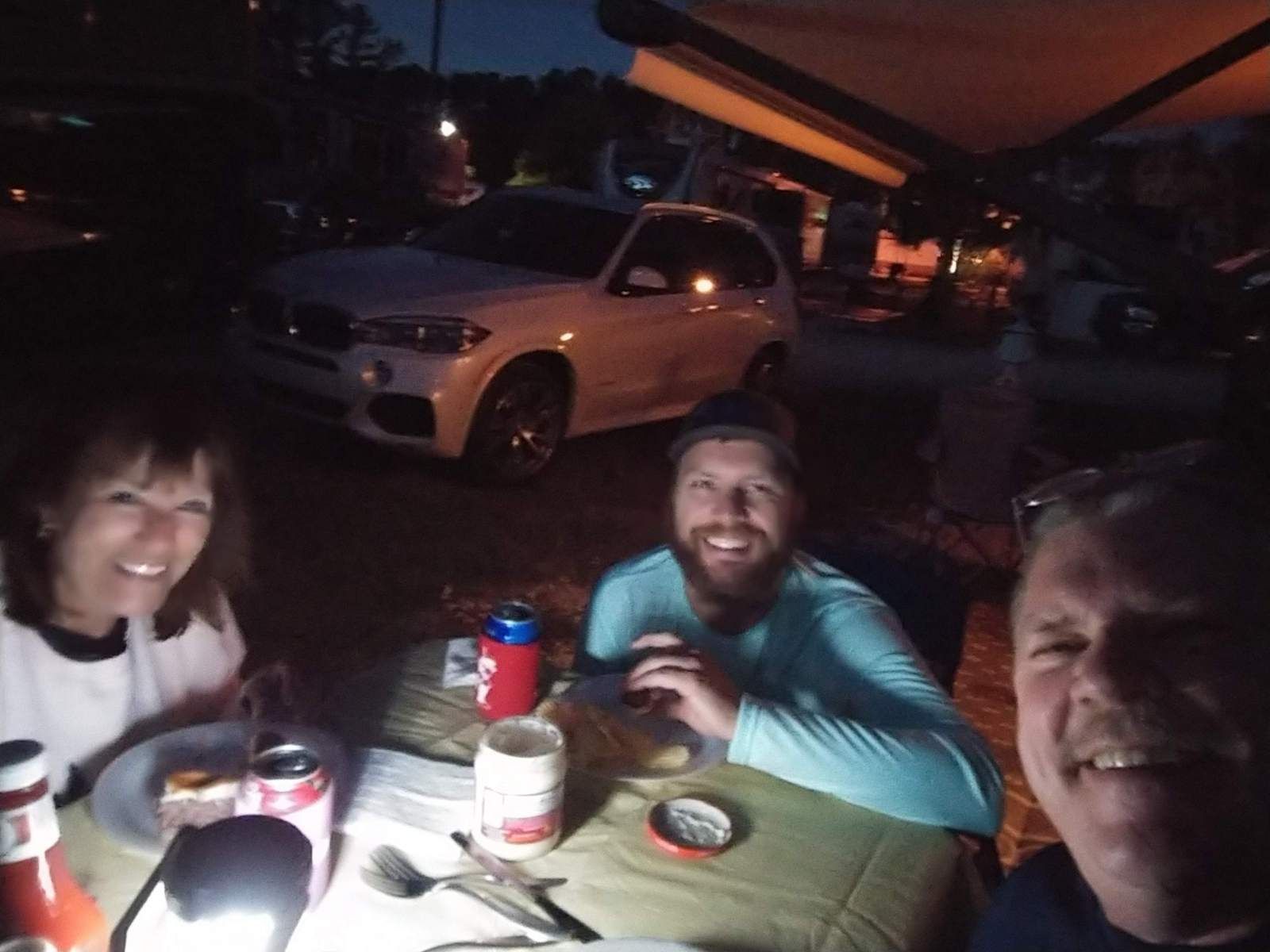 A group of people are sitting at a table with a car in the background