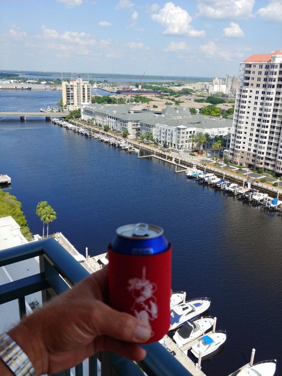 A person is holding a can of beer on a balcony overlooking a body of water