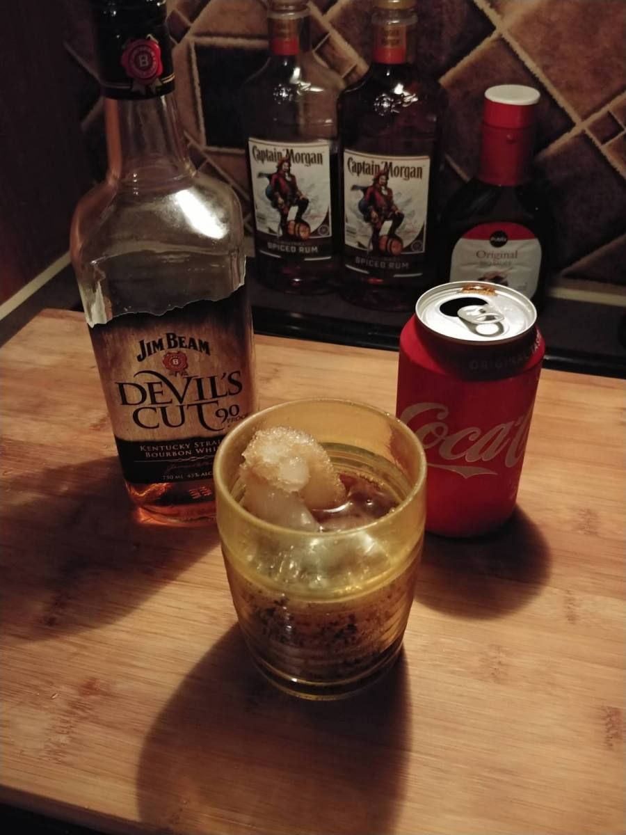 A bottle of devil 's cut next to a can of coke