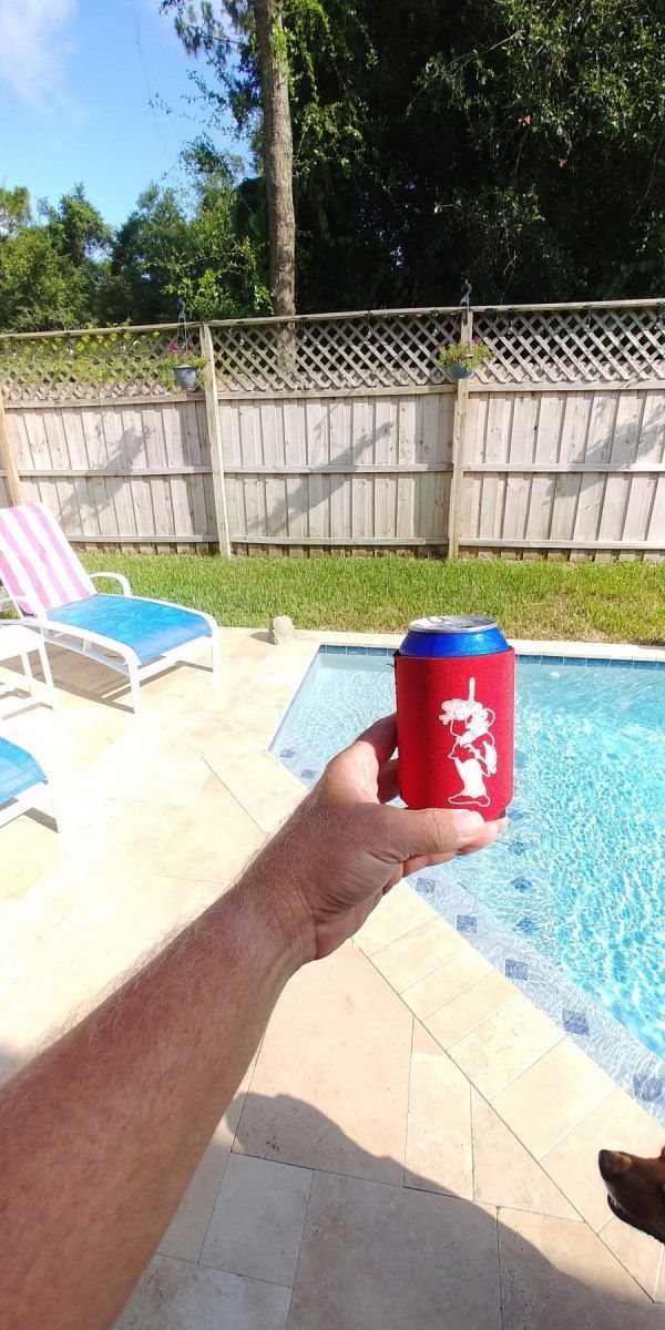 A person is holding a can of beer in front of a swimming pool.