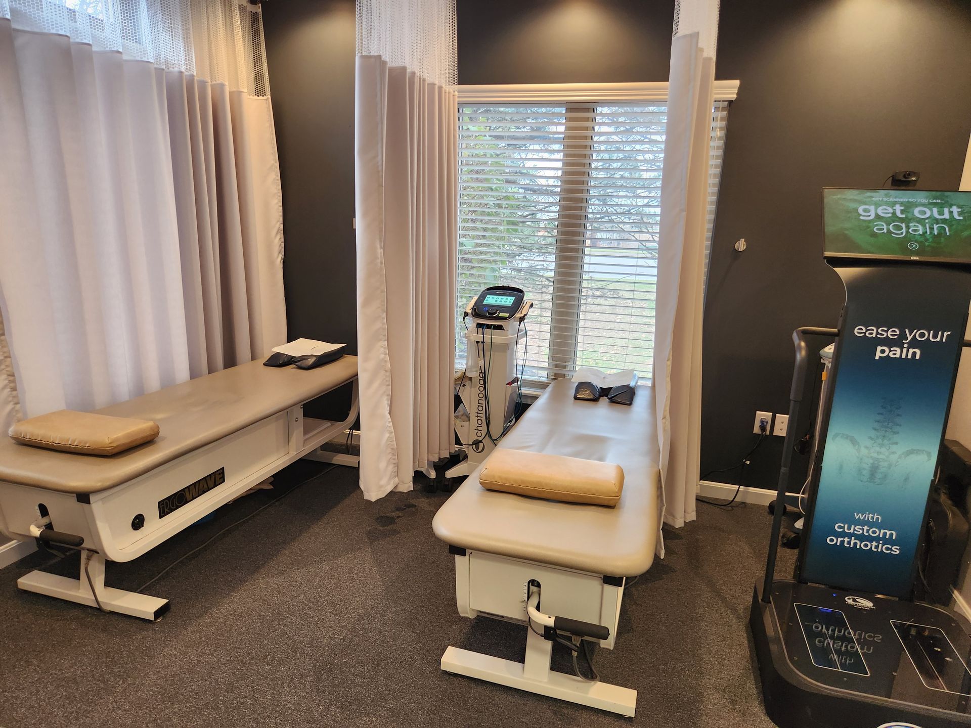 Two therapy tables in a treatment room, with a window and a medical device. Two therapy tables in a treatment room, with a window and a medical device.