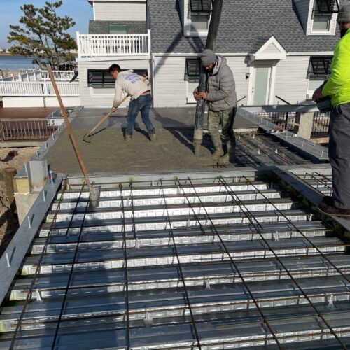 Two Men are Working on a Concrete Floor in Front of a House — Ocean City, NJ — Padula Masonry
