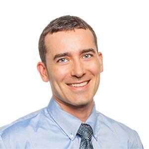 A man in a blue shirt and tie is smiling for the camera.