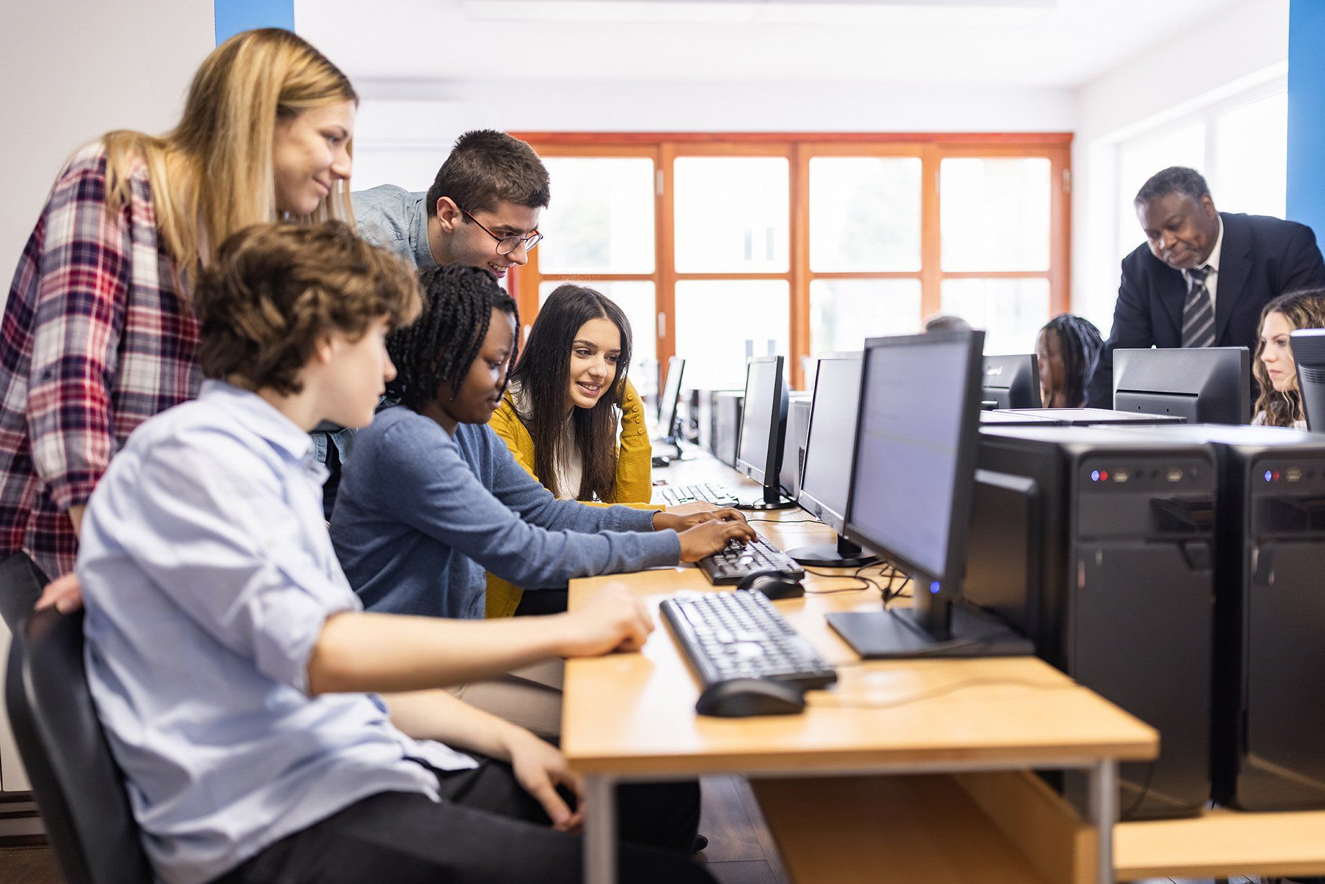 A group of people are looking at a computer screen in a computer lab.
