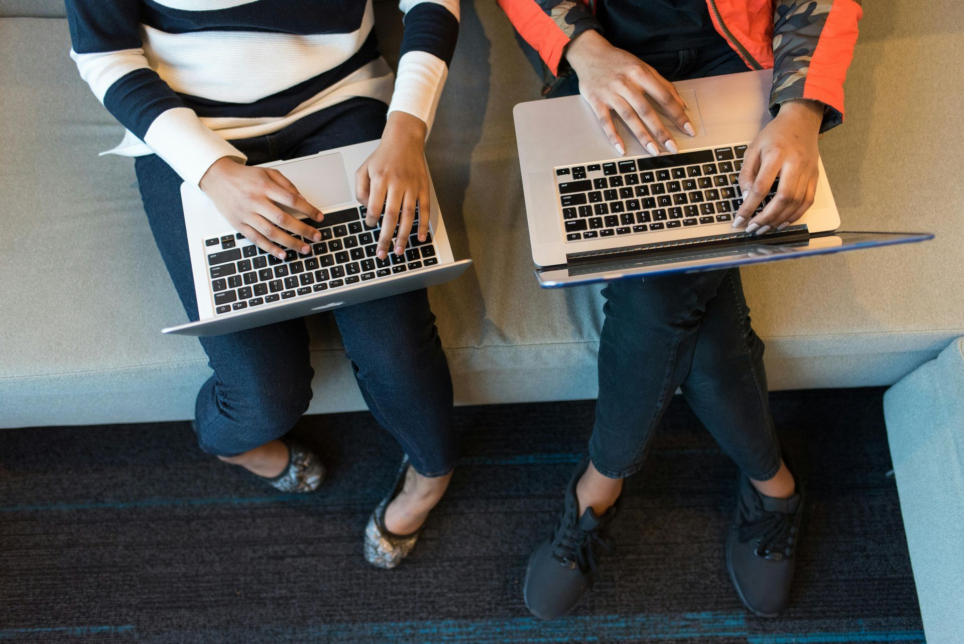 Two people are sitting on a couch using laptops