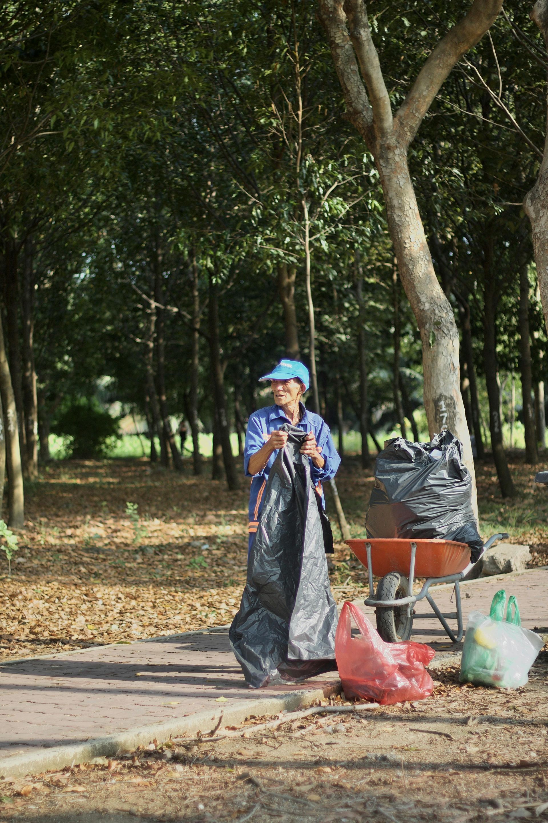 A man standing next to a wheelbarrow full of trash bags