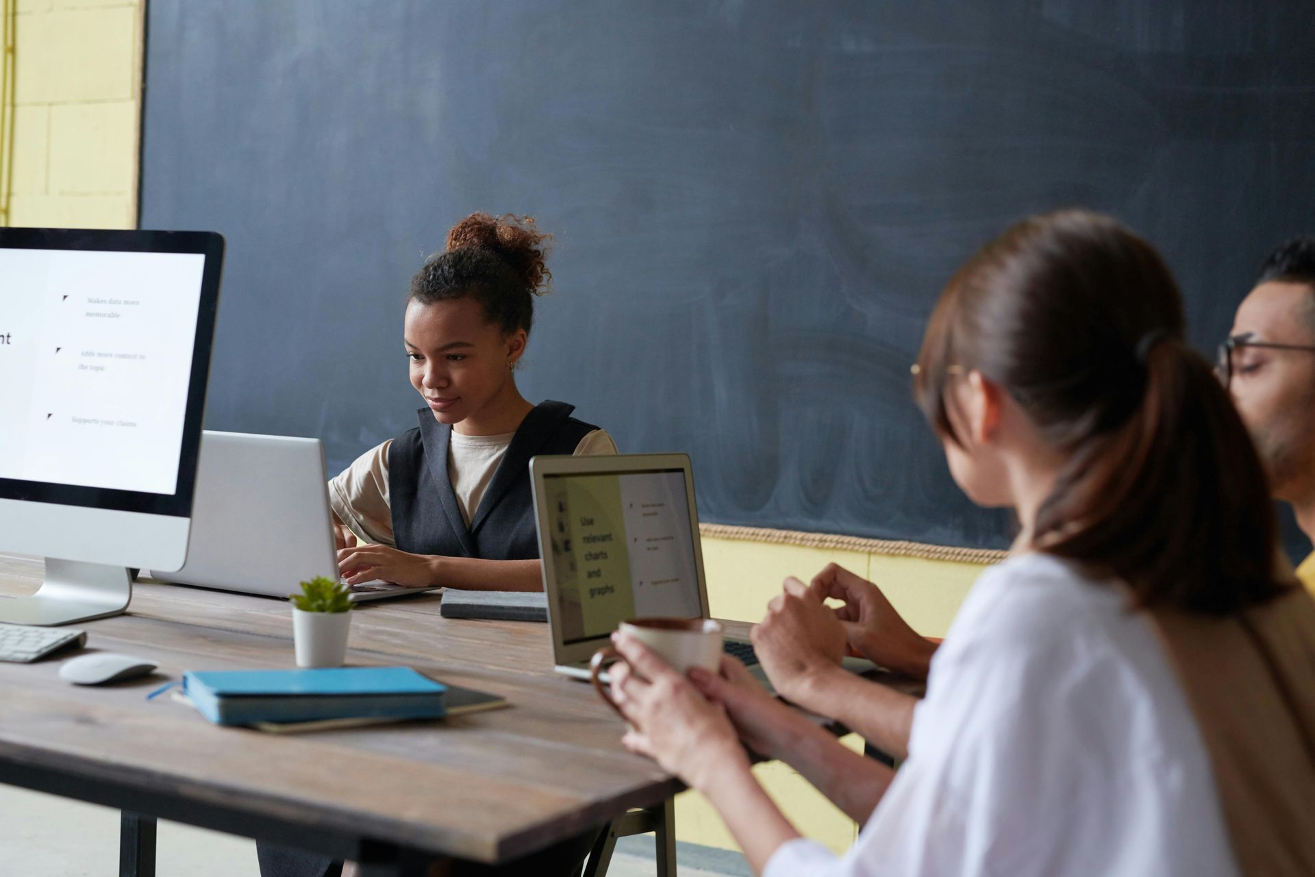 A group of people are sitting around a table with computers and laptops