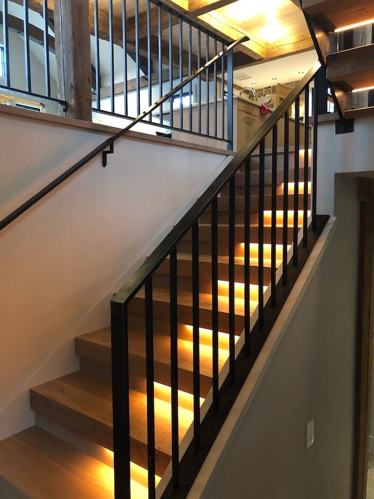 A wooden staircase with a metal railing and lights on the steps
