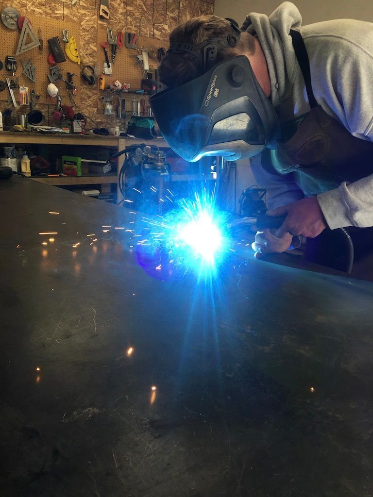 A man wearing a welding mask is welding a piece of metal