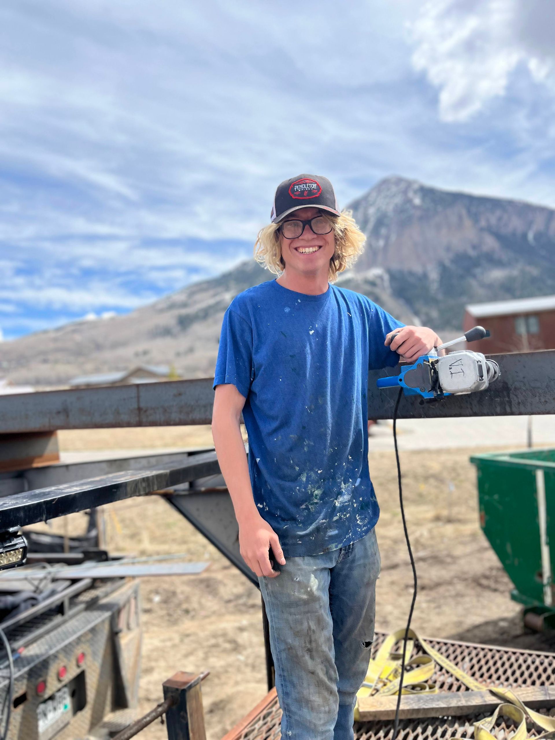 A man in a blue shirt is standing in front of a mountain holding a tool.