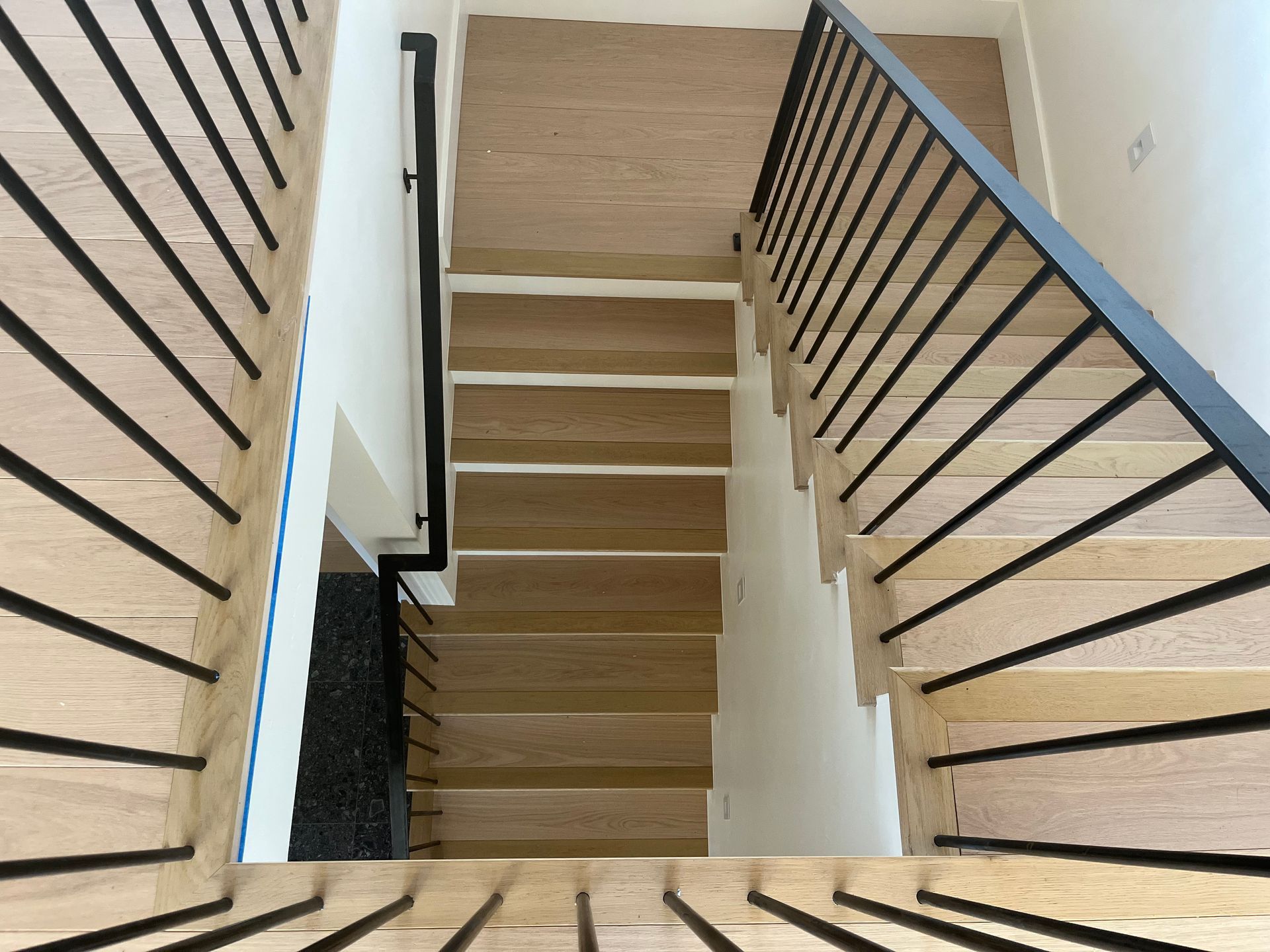 A view of a wooden staircase with a black railing.