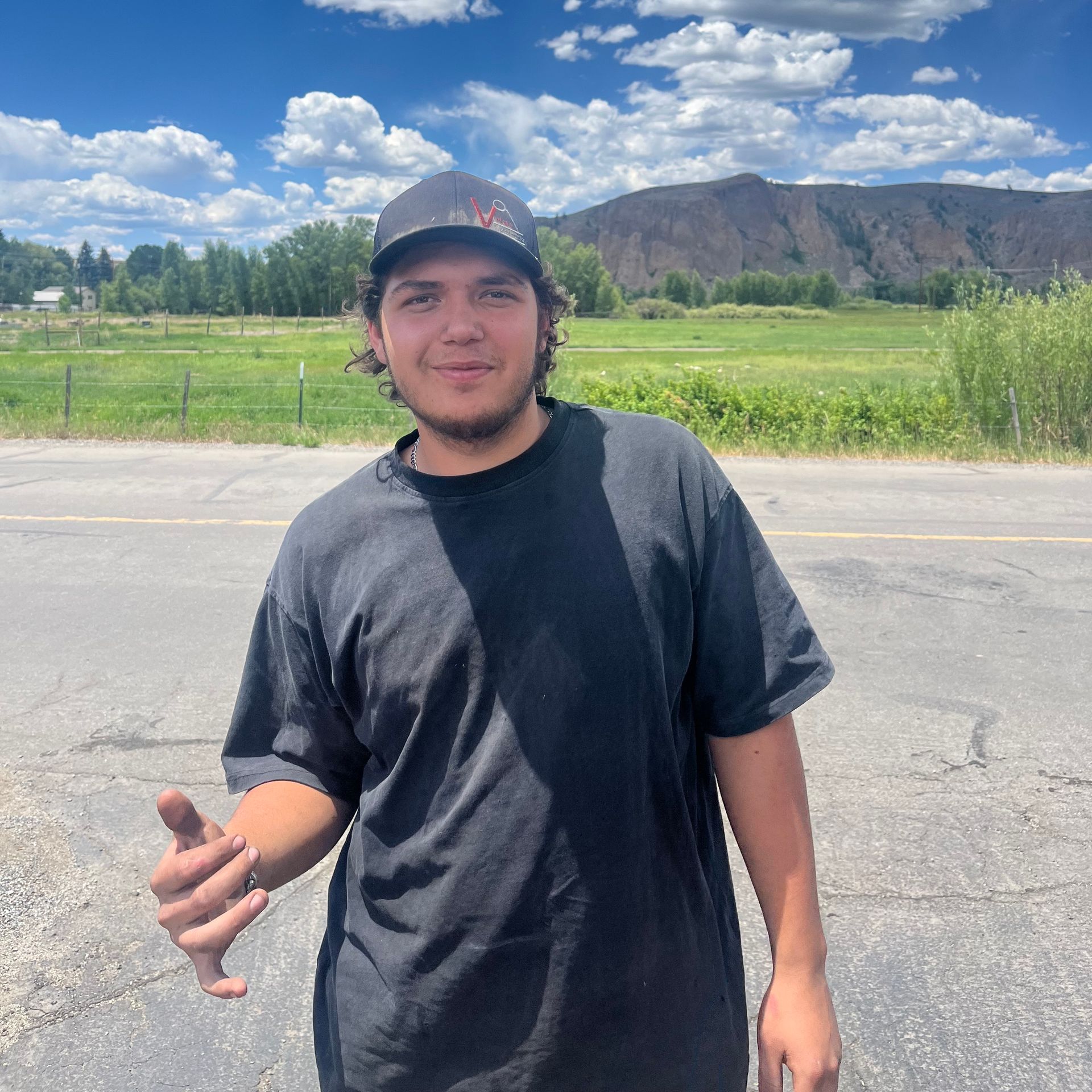 A man wearing a hat and a black shirt is standing on the side of the road
