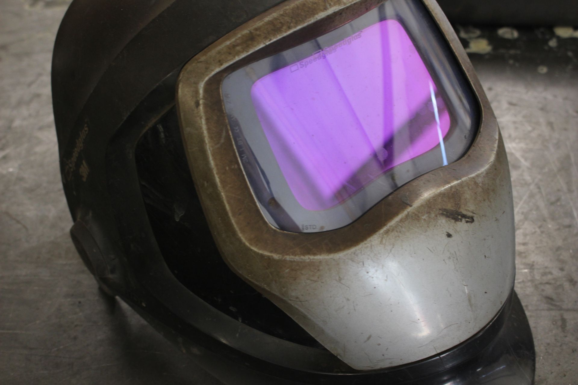 A close up of a welding helmet with a purple lens on a table.