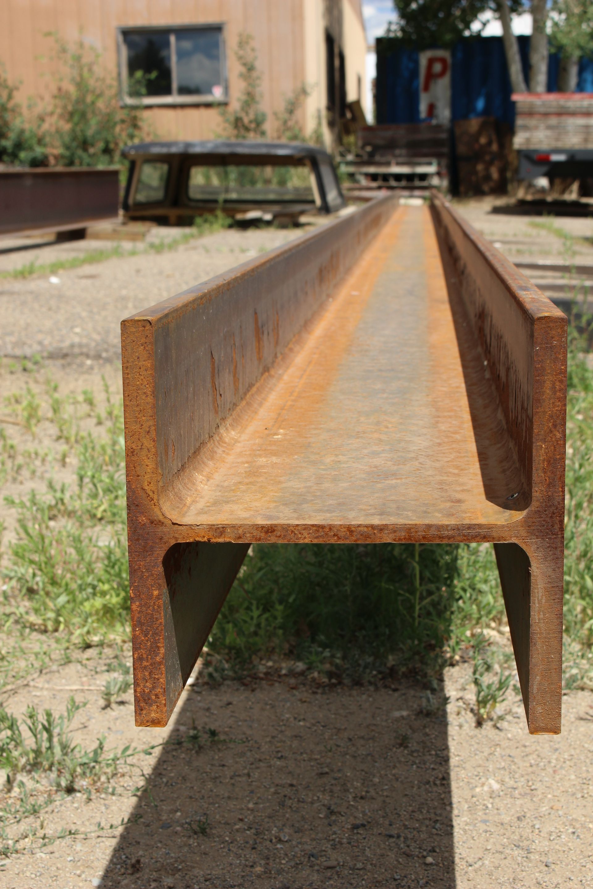 A rusty metal beam is sitting on the ground in front of a building.