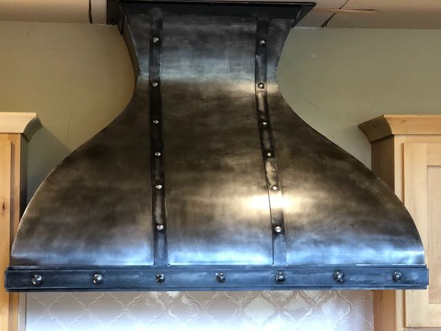A stainless steel hood is hanging from the ceiling in a kitchen.