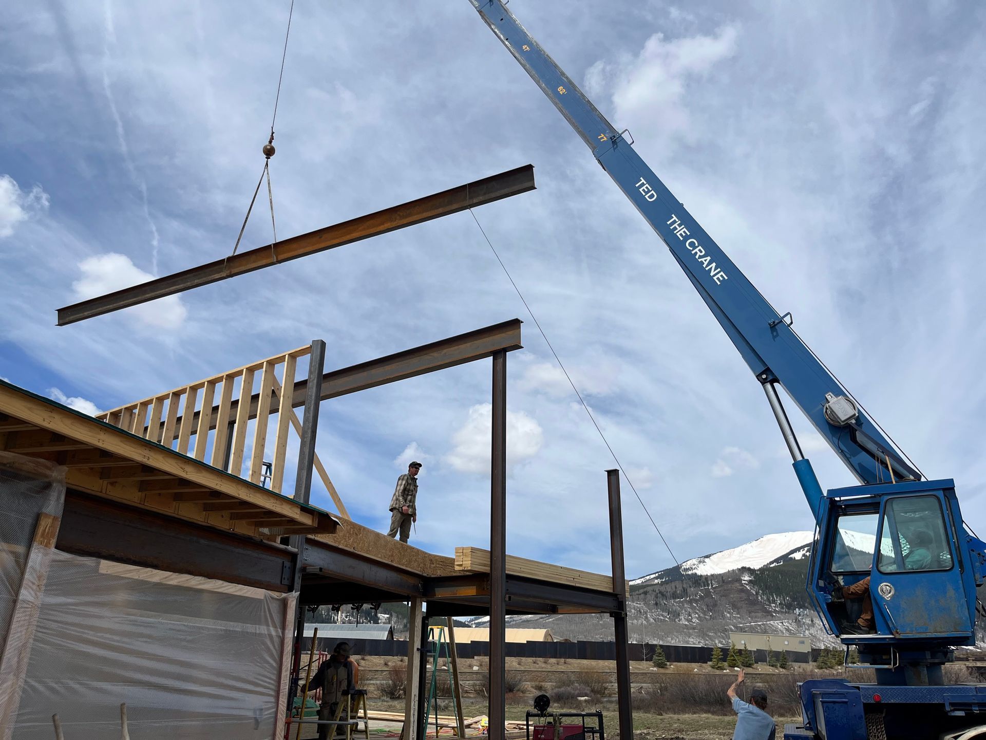 A blue crane is lifting a beam on top of a building under construction.