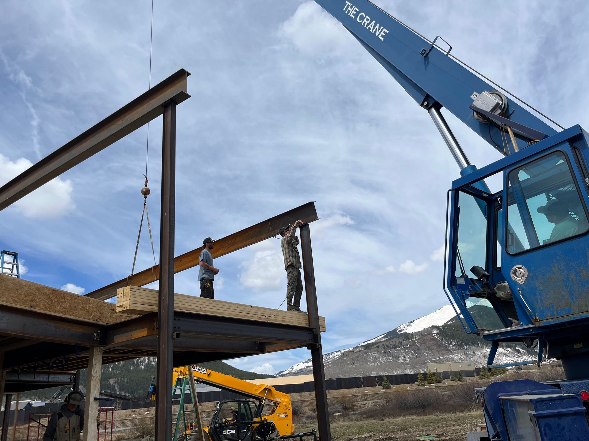 A blue crane is lifting a beam on top of a building under construction.