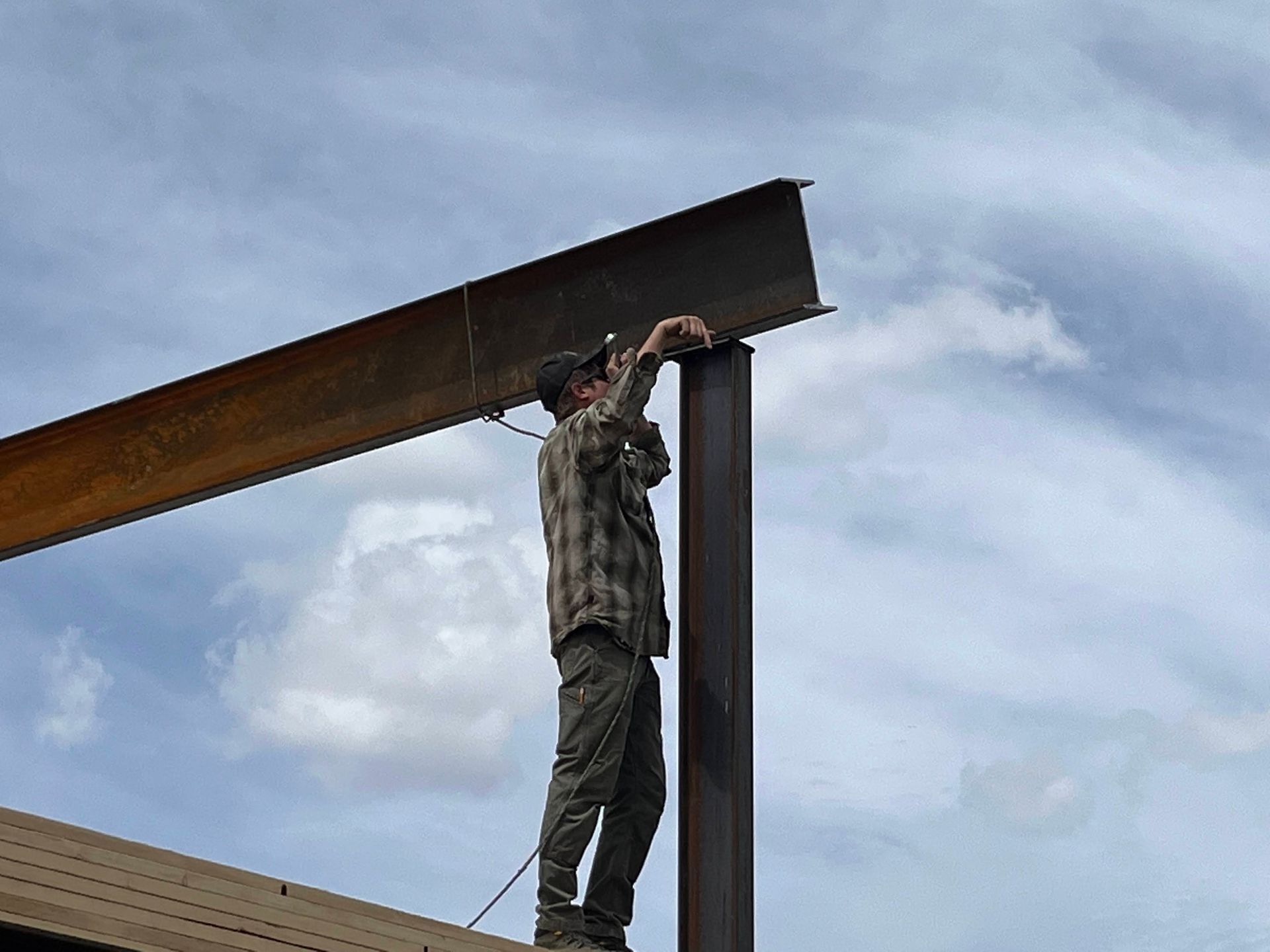 A man in a plaid shirt is working on a metal structure.