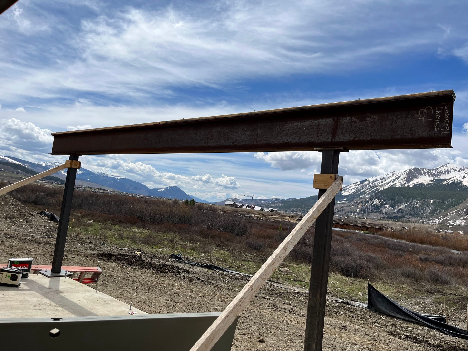 A large metal beam is sitting in the middle of a dirt field with mountains in the background