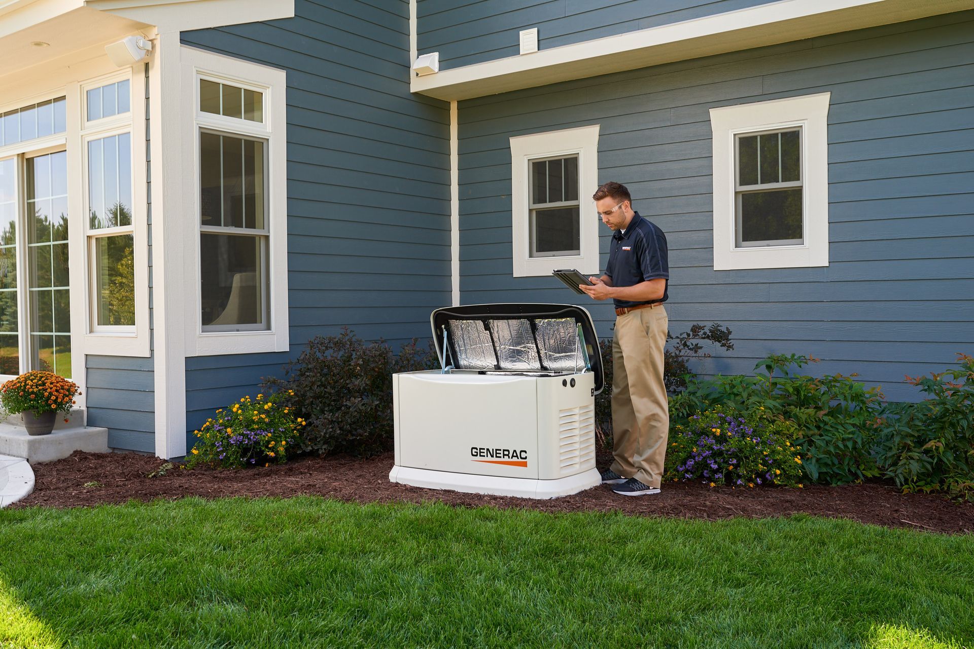 Man inspecting a generator near a blue house with white trim; outdoors, sunny day.