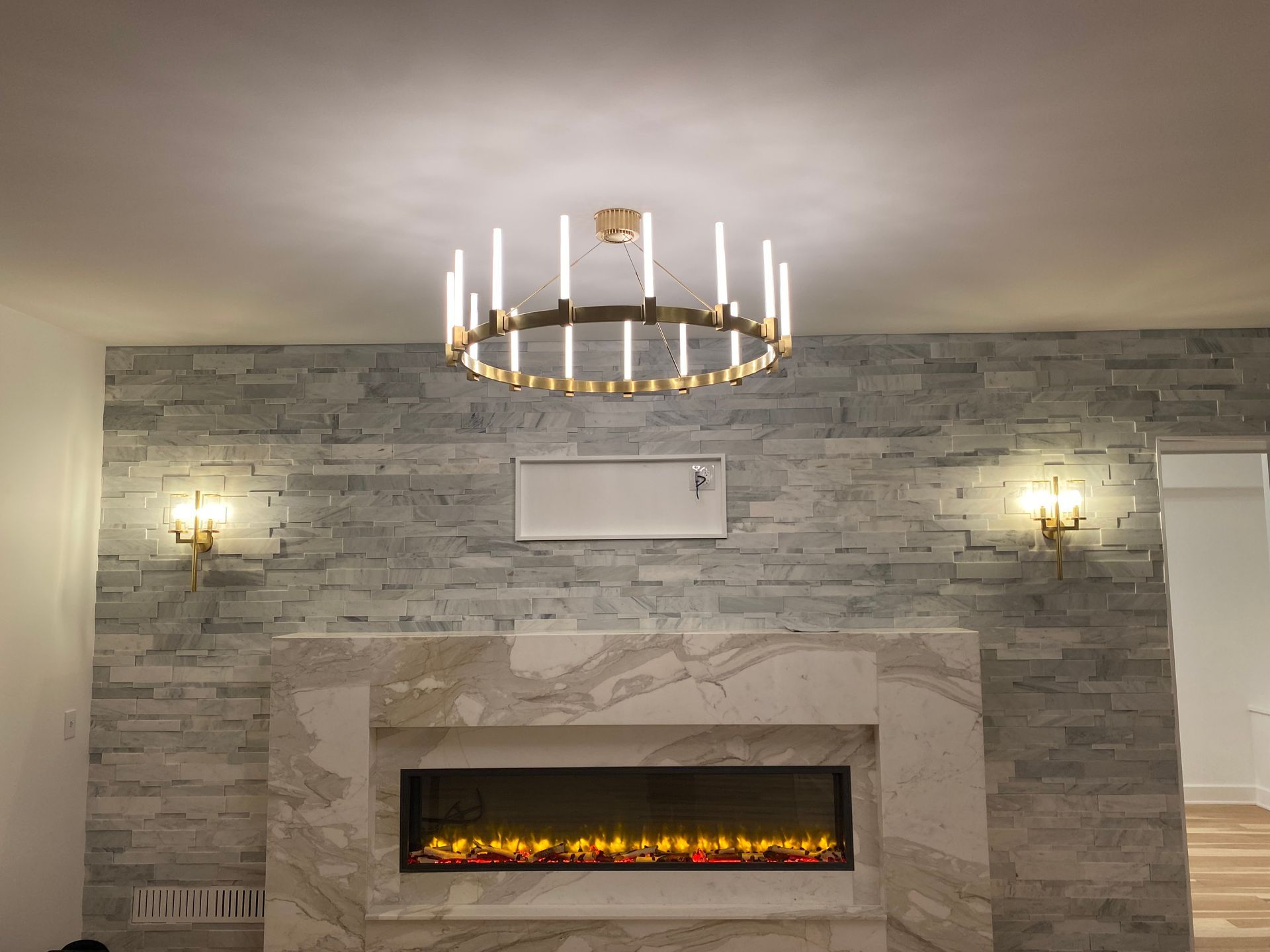 Fireplace with a stone accent wall, gold chandelier, and sconces.