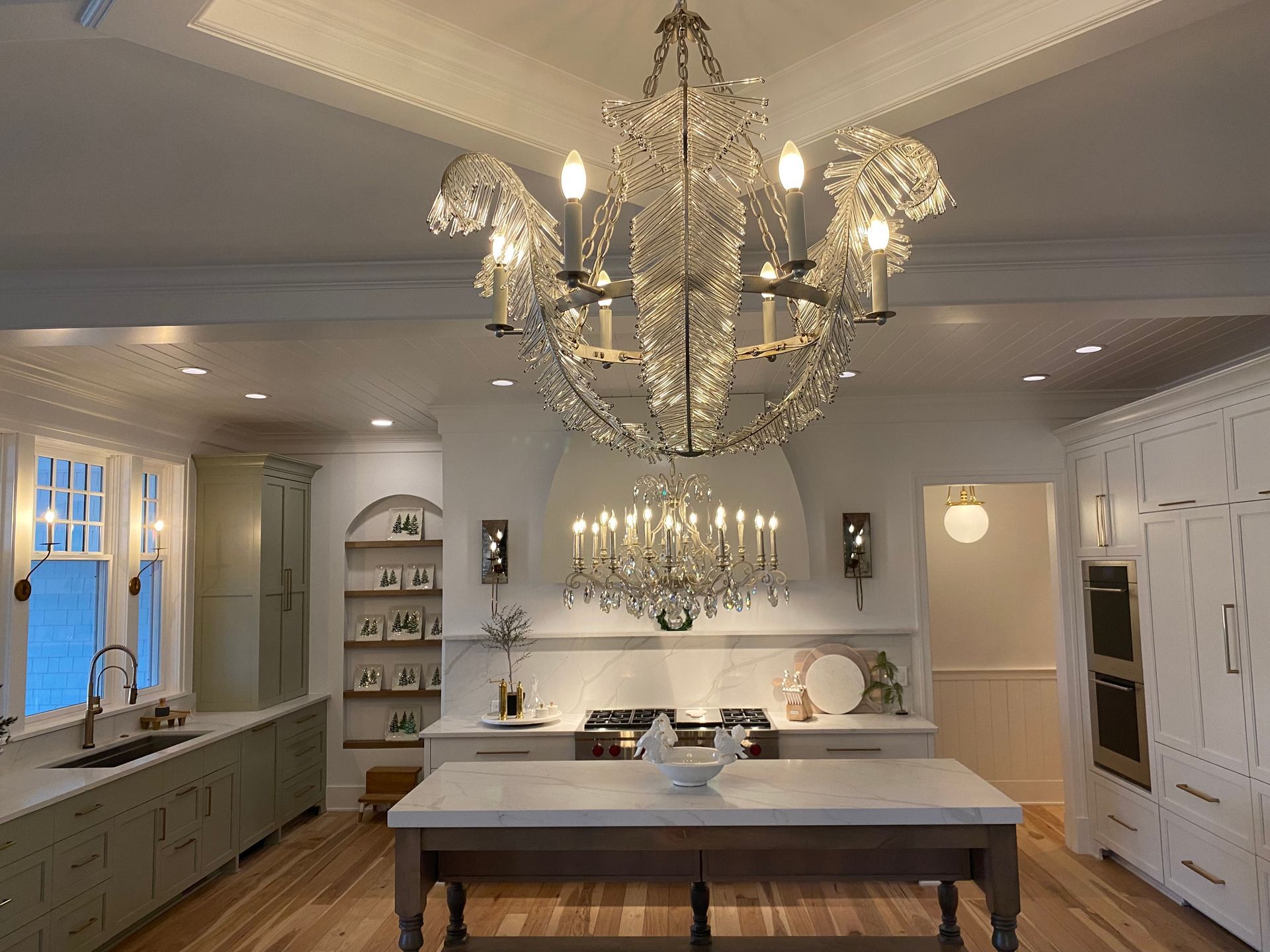 Elegant kitchen with two crystal chandeliers, island, and cabinets.