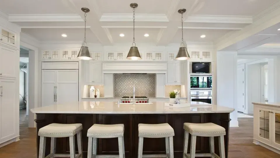 Kitchen with island, pendant lights, white cabinets, dark wood island base, and four stools.