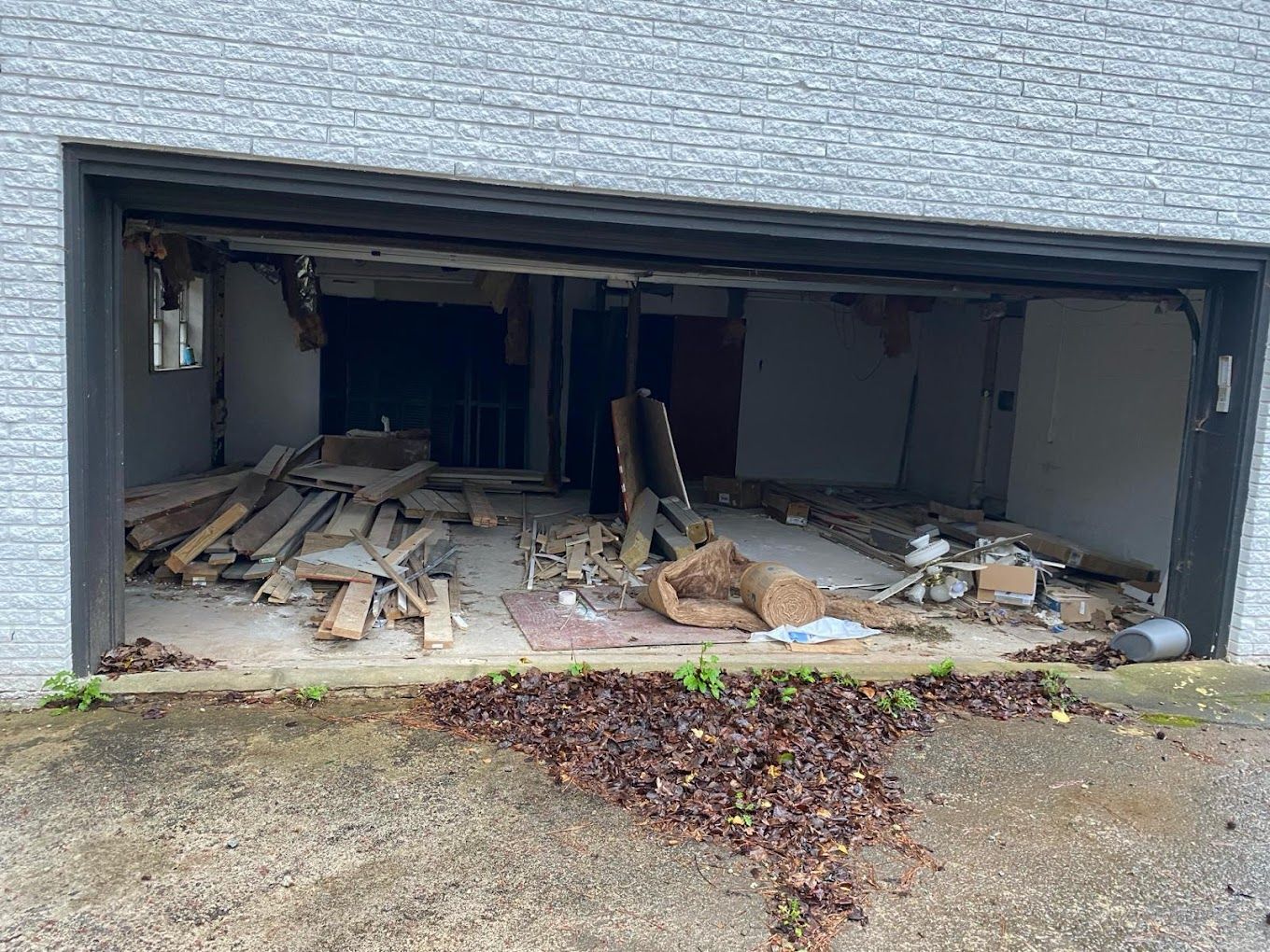 The garage door is open and there is a lot of wood in it.