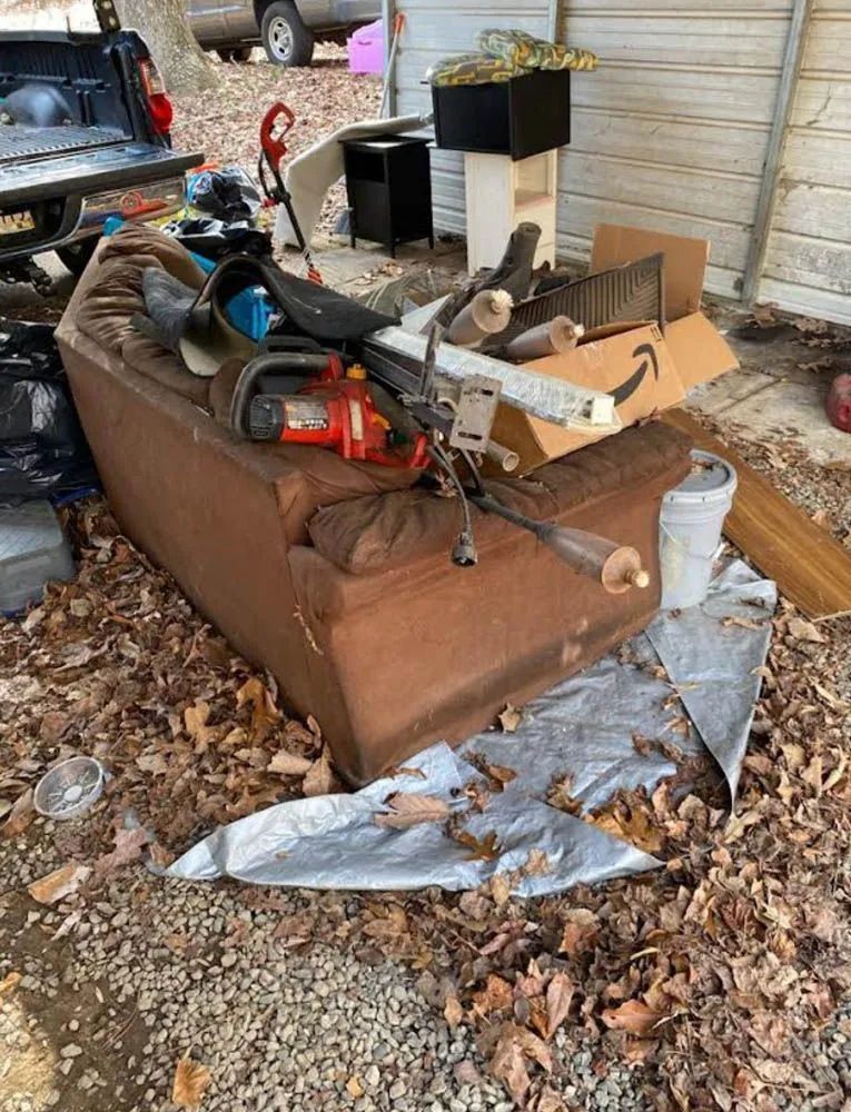 A brown couch is sitting on top of a pile of trash.