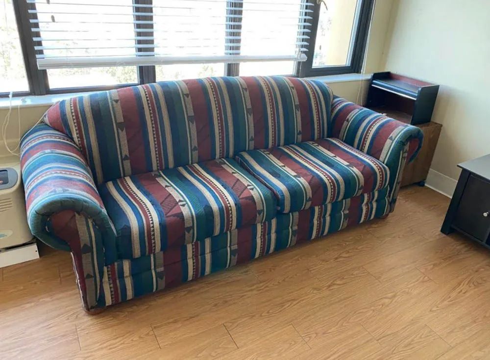 A striped couch is sitting in a living room next to a window.