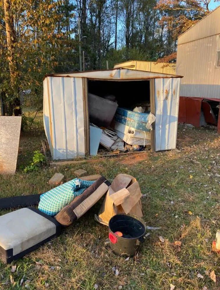 A shed filled with junk is sitting in the grass next to a house.