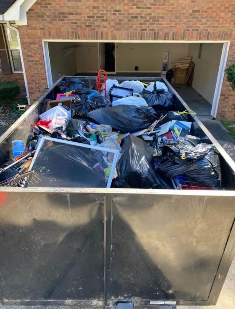 A dumpster filled with trash is parked in front of a brick house.