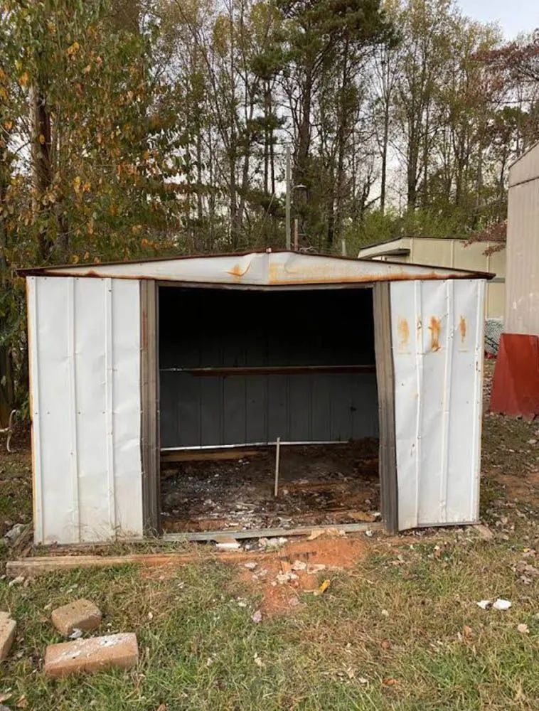 A white metal shed is sitting in the middle of a grassy field.
