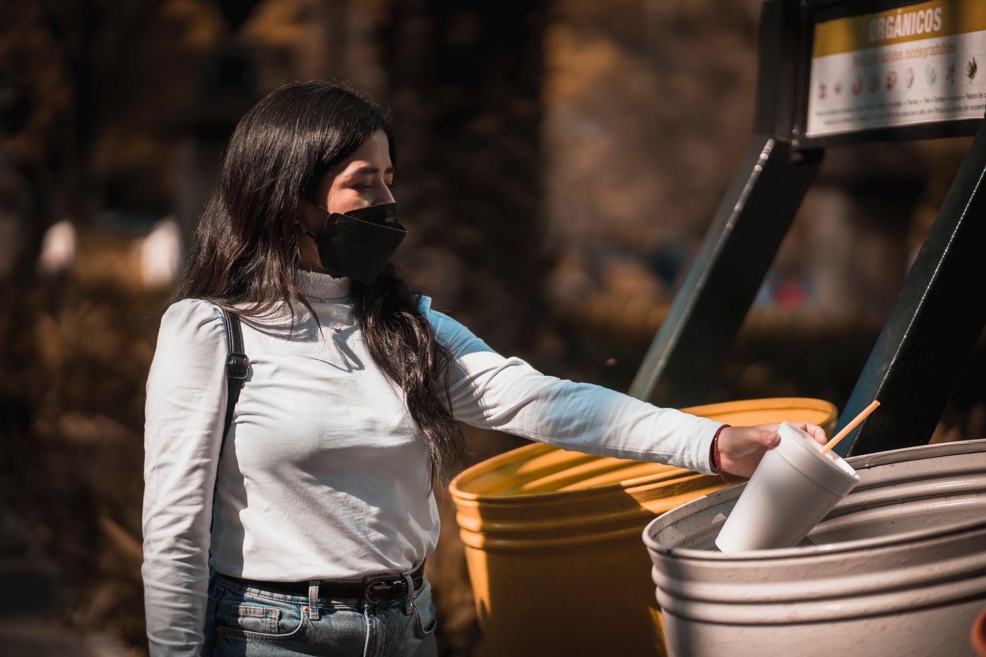 mujer con mascarilla tirando un vaso de plástico en contenedores de basura