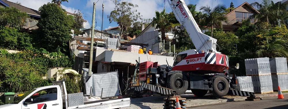 A large crane is sitting on the side of the road next to a white truck.