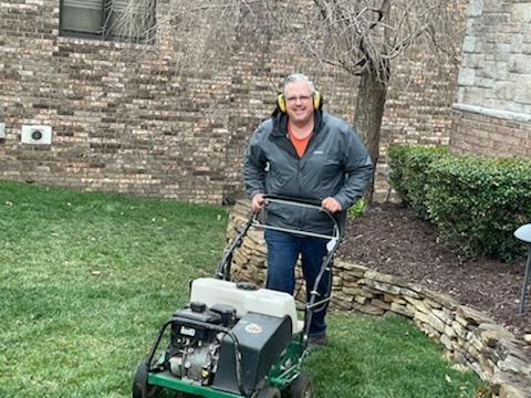 A man is standing next to a lawn mower in a yard.