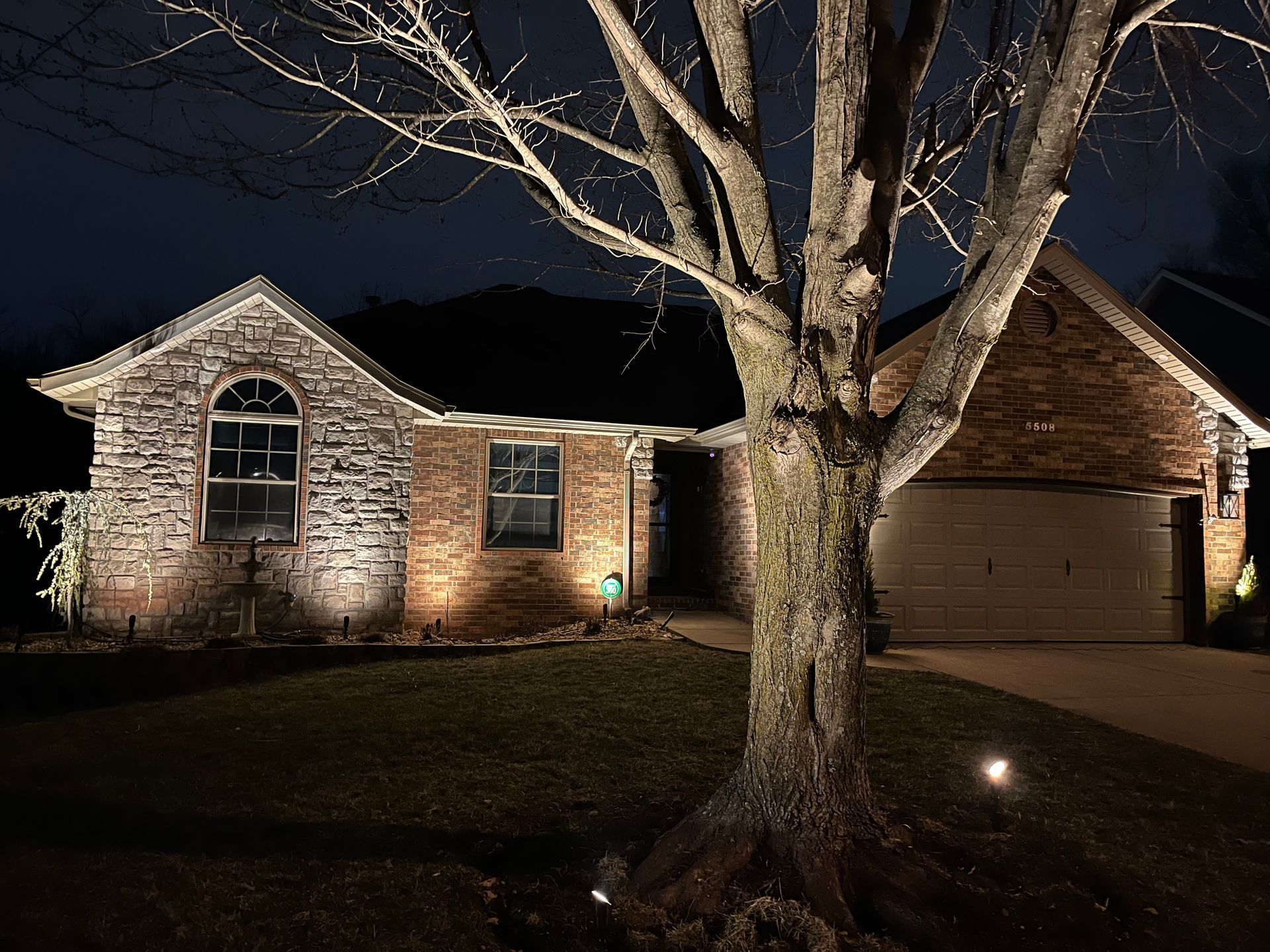 A brick house is lit up at night with a tree in front of it