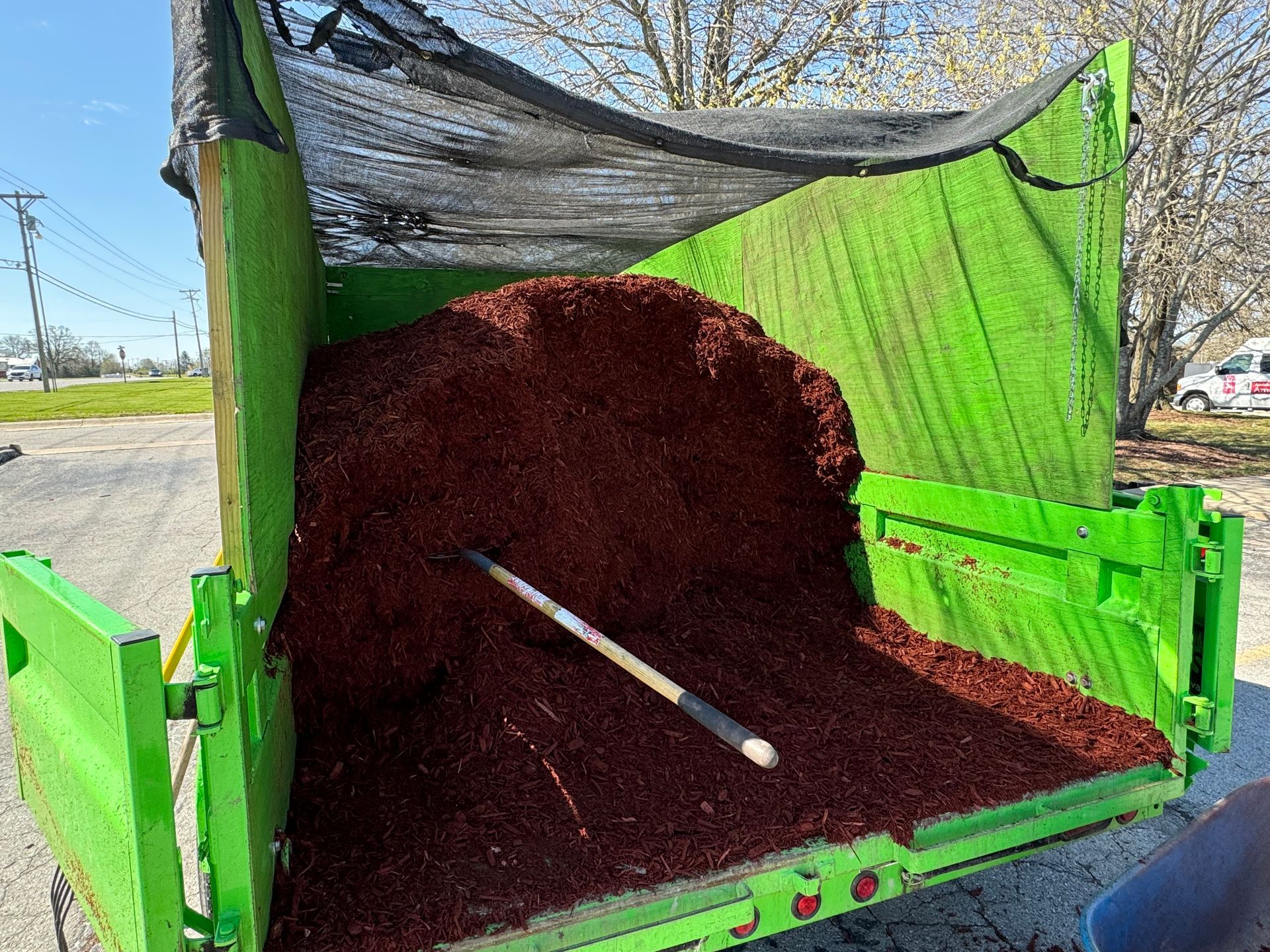 A green trailer filled with brown mulch and a shovel