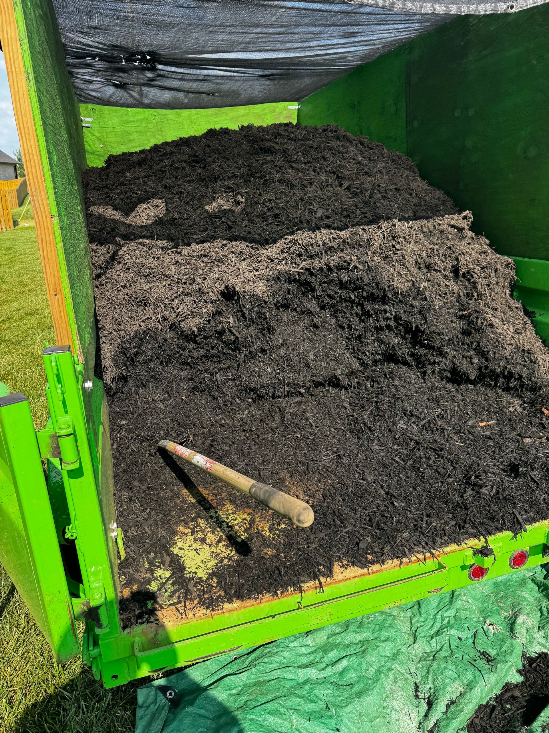 A green dumpster filled with dirt and a shovel
