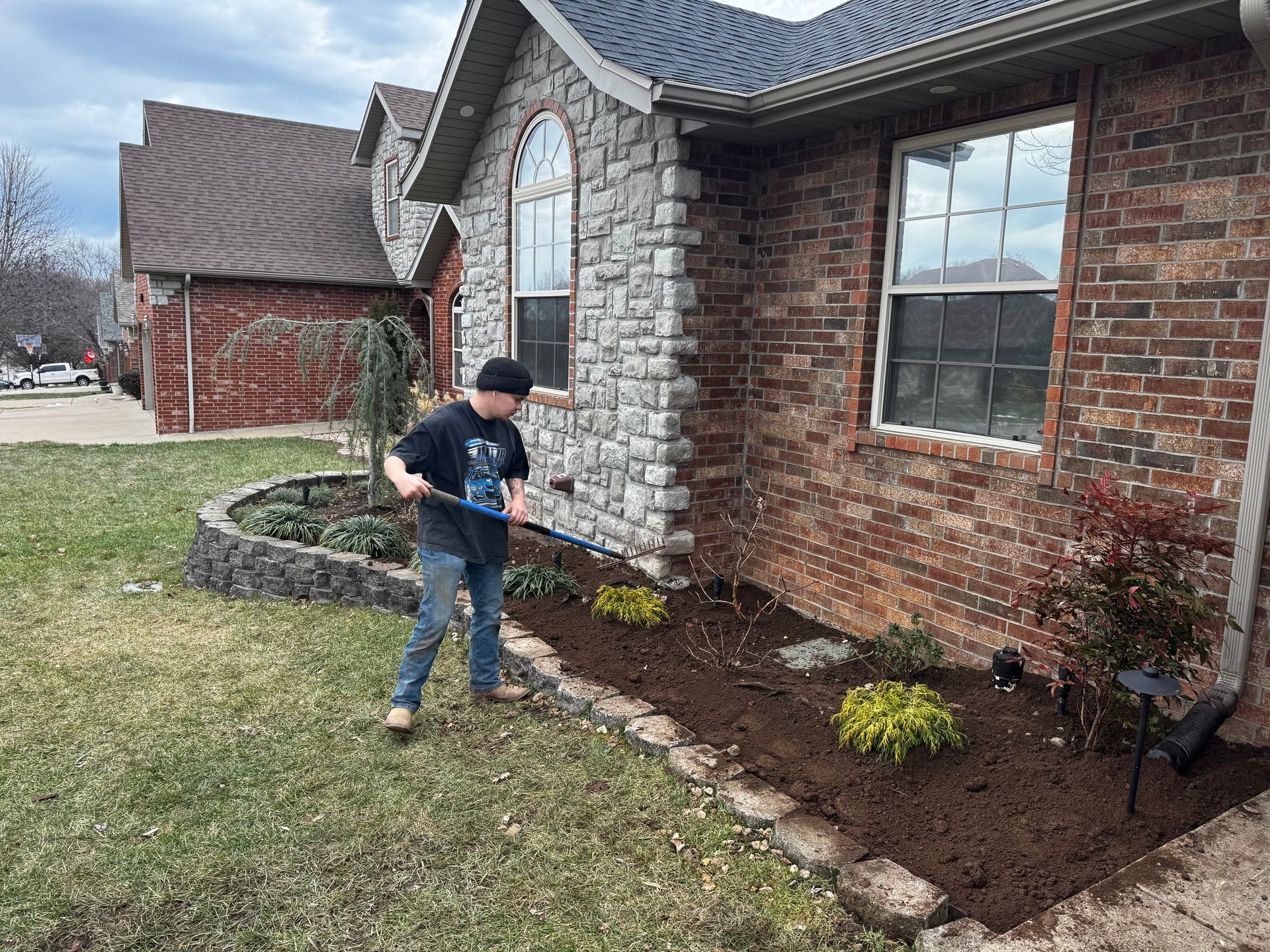 A boy is watering plants in front of a brick house