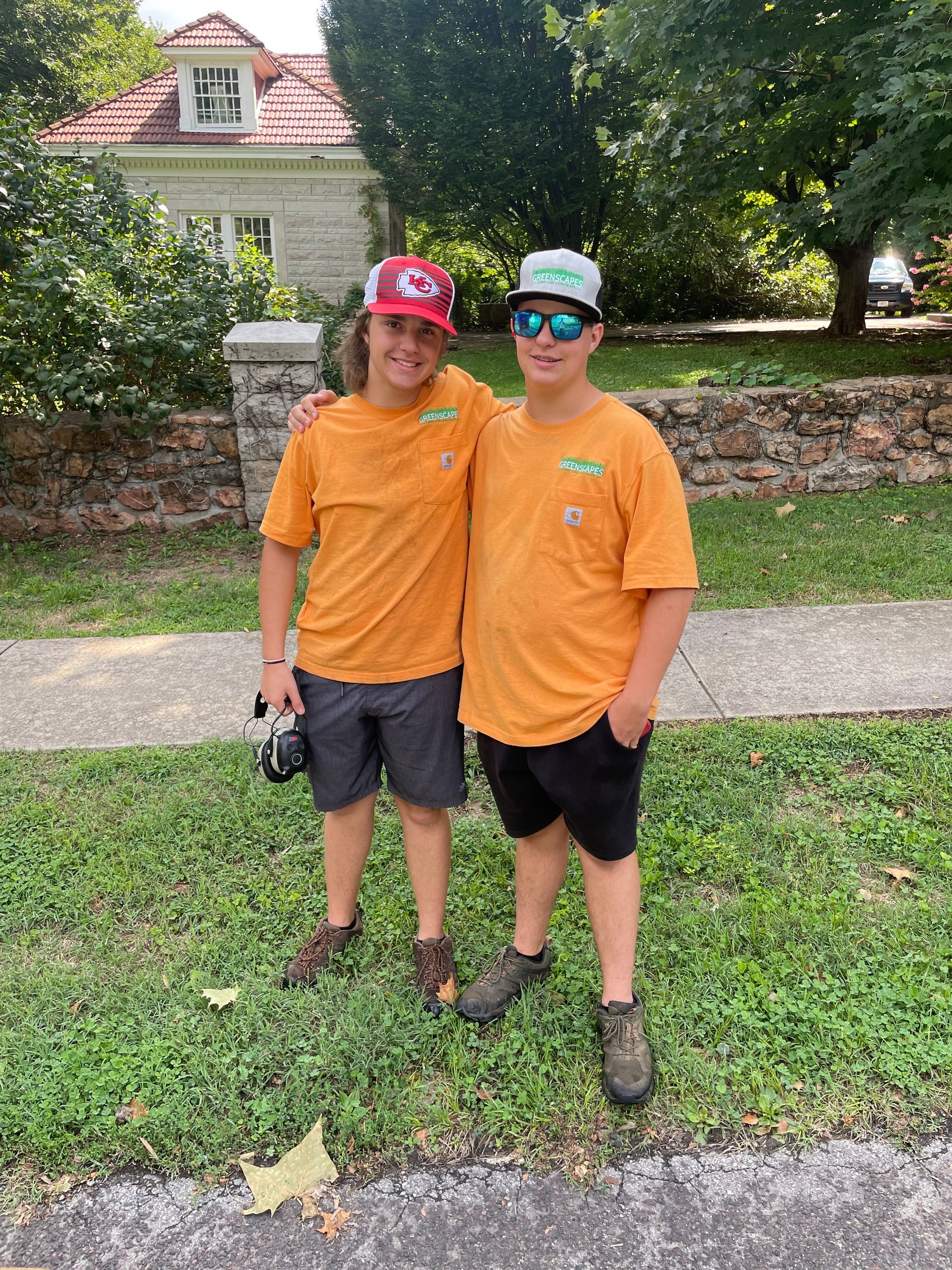 Two young men are posing for a picture in front of a house