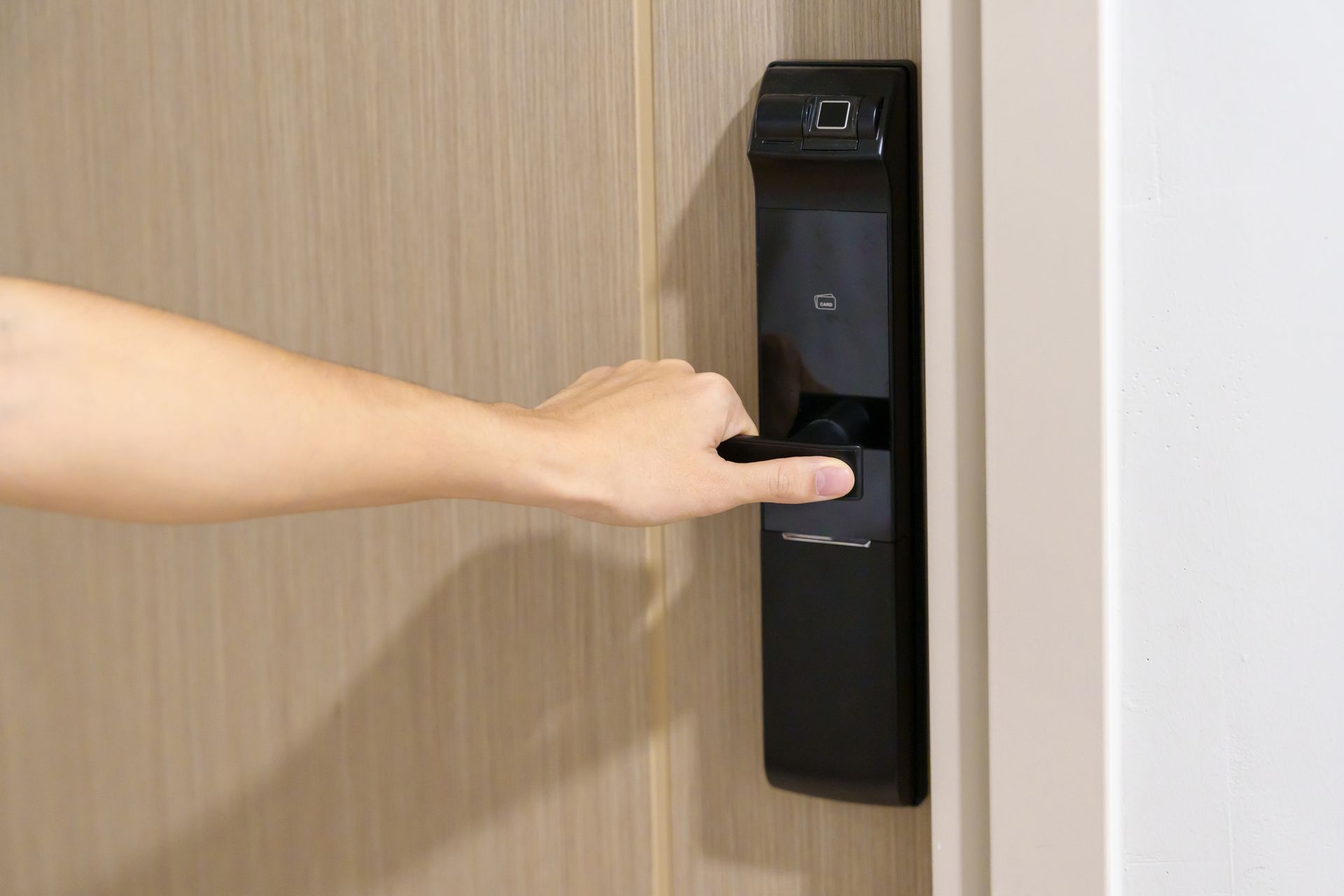 Person's Hand Opening a Modern Black Door With a Fingerprint Reader on a Light Wood Door — North East Locksmiths in Wodonga, VIC