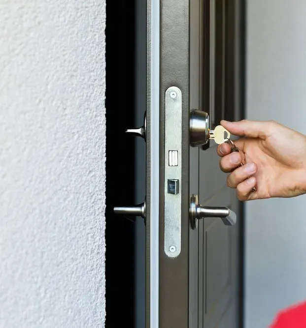 Person unlocking a dark door with a key, close-up. Focus is on the hand and lock. — North East Locksmiths in Albury, NSW